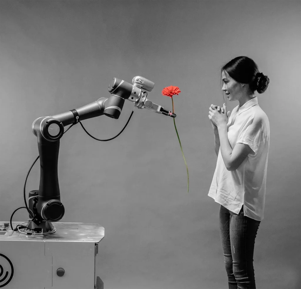 Un bras robotique offrant une fleur rouge à une femme souriante, illustrant l’interaction entre la technologie et l’humain.