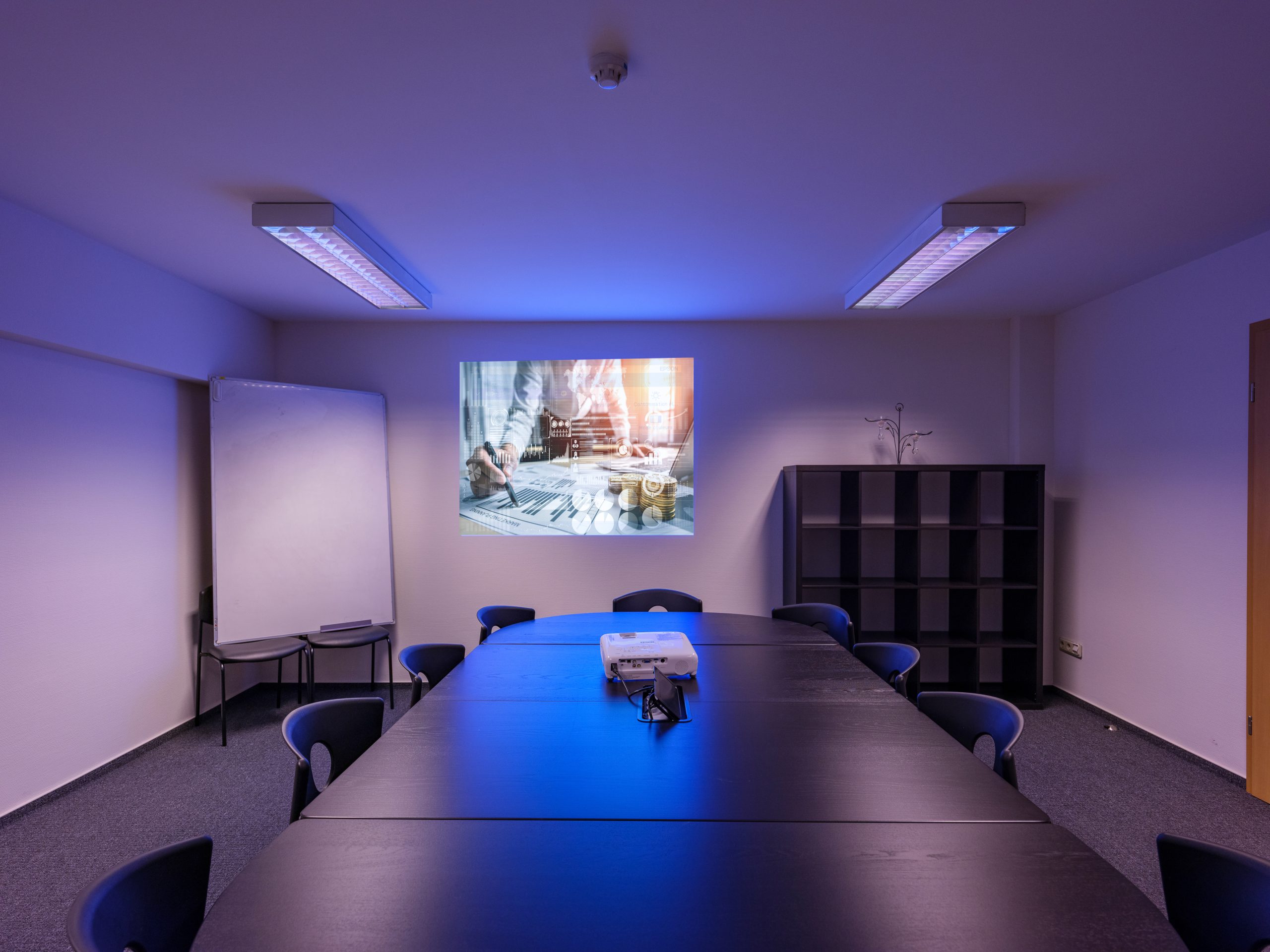 Salle de réunion moderne avec table de conférence, projecteur et ambiance lumineuse bleutée.