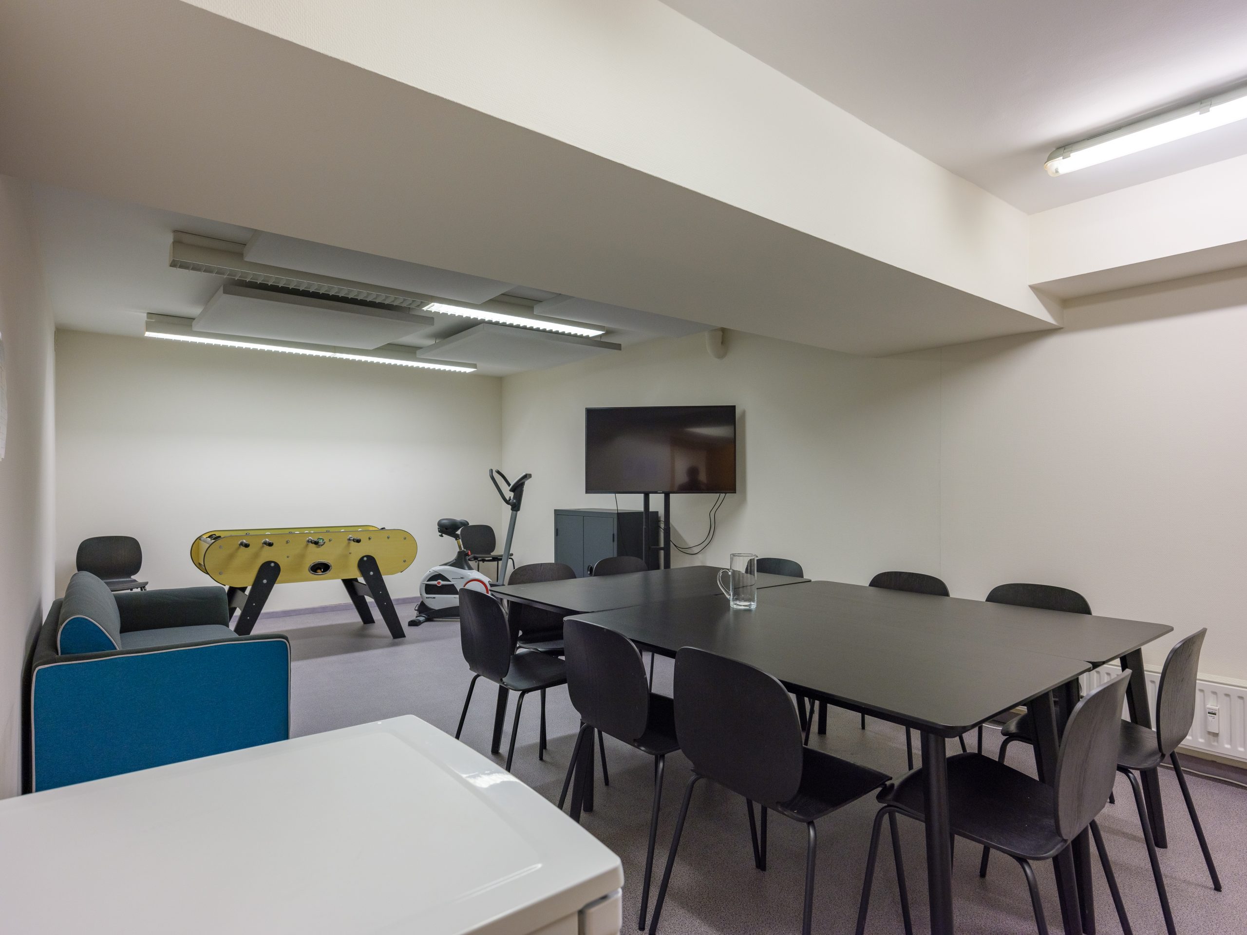 Salle de détente et de réunion équipée d’un baby-foot, d’un téléviseur et d’un espace de travail moderne.